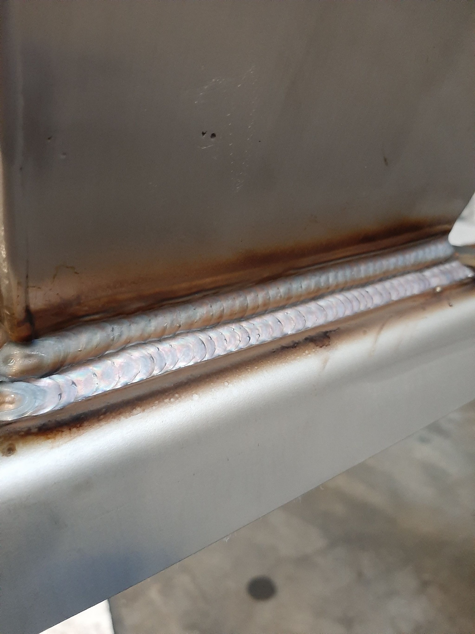 Szczegółowe zbliżenie na świeży spaw na metalowej konstrukcji, widoczne regularne ślady po spawaniu i lekkie przebarwienia termiczne.