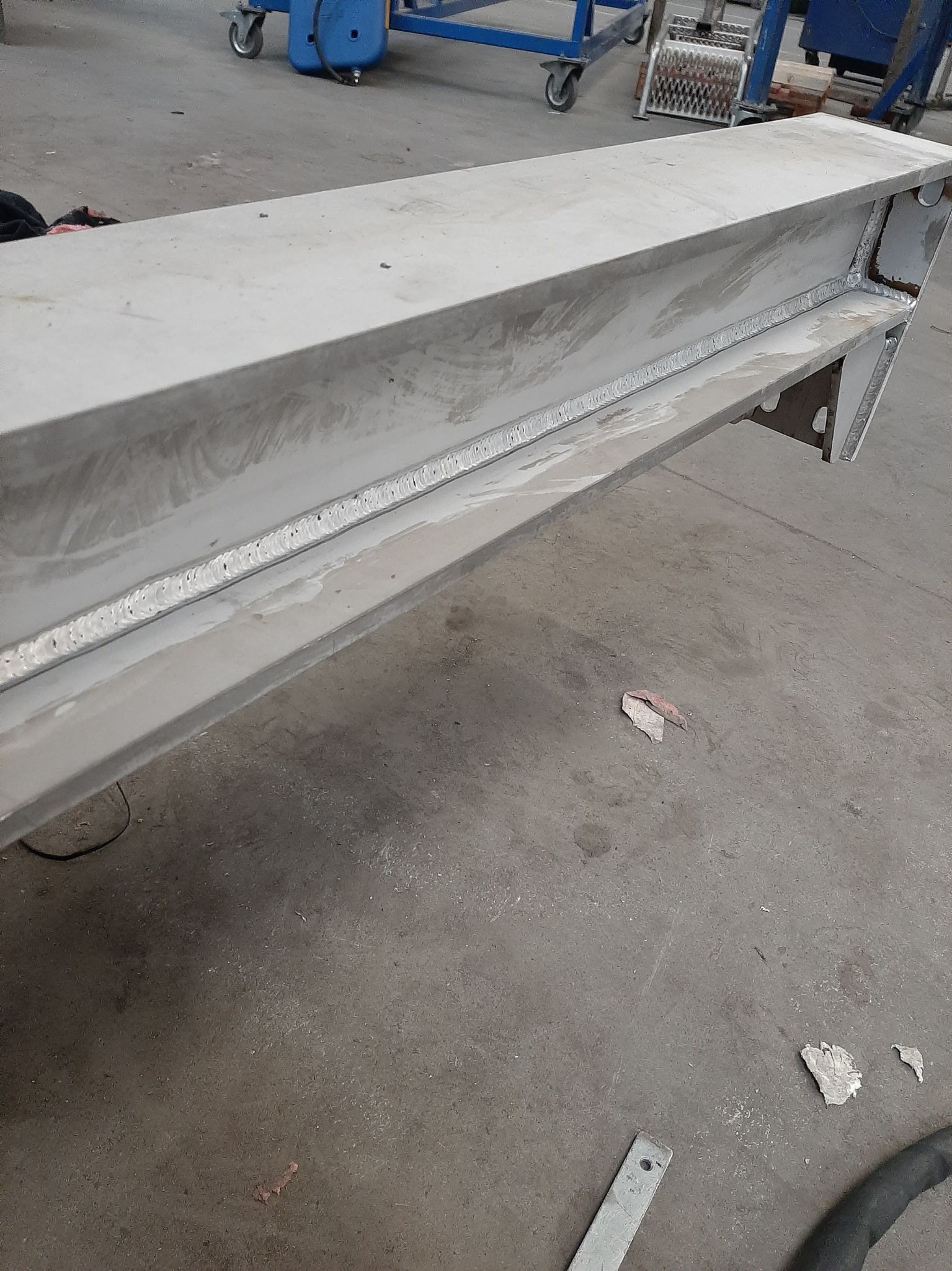 Szlifowana, spawana belka stalowa o przekroju dwuteowym, widoczne ślady obróbki i spawania, na podłodze fragmenty metalu po obróbce.