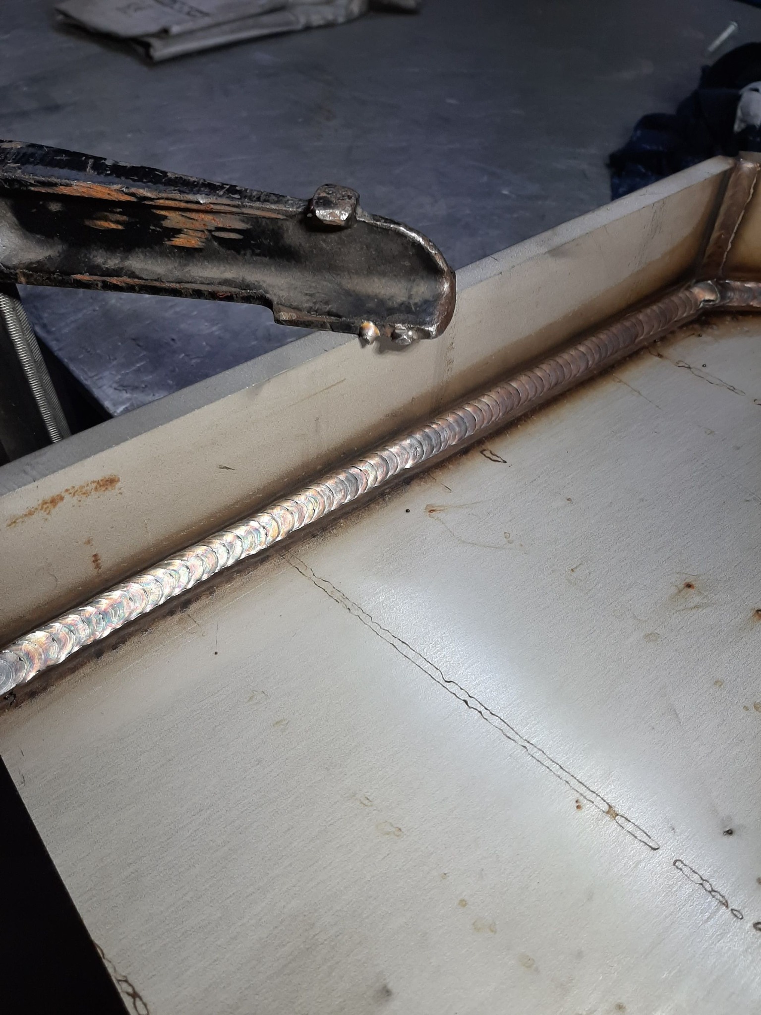 Detal z procesu spawania metalowej konstrukcji, widoczny świeży spaw o opalizującym zabarwieniu oraz uchwyt spawalniczy w górnej części kadru.