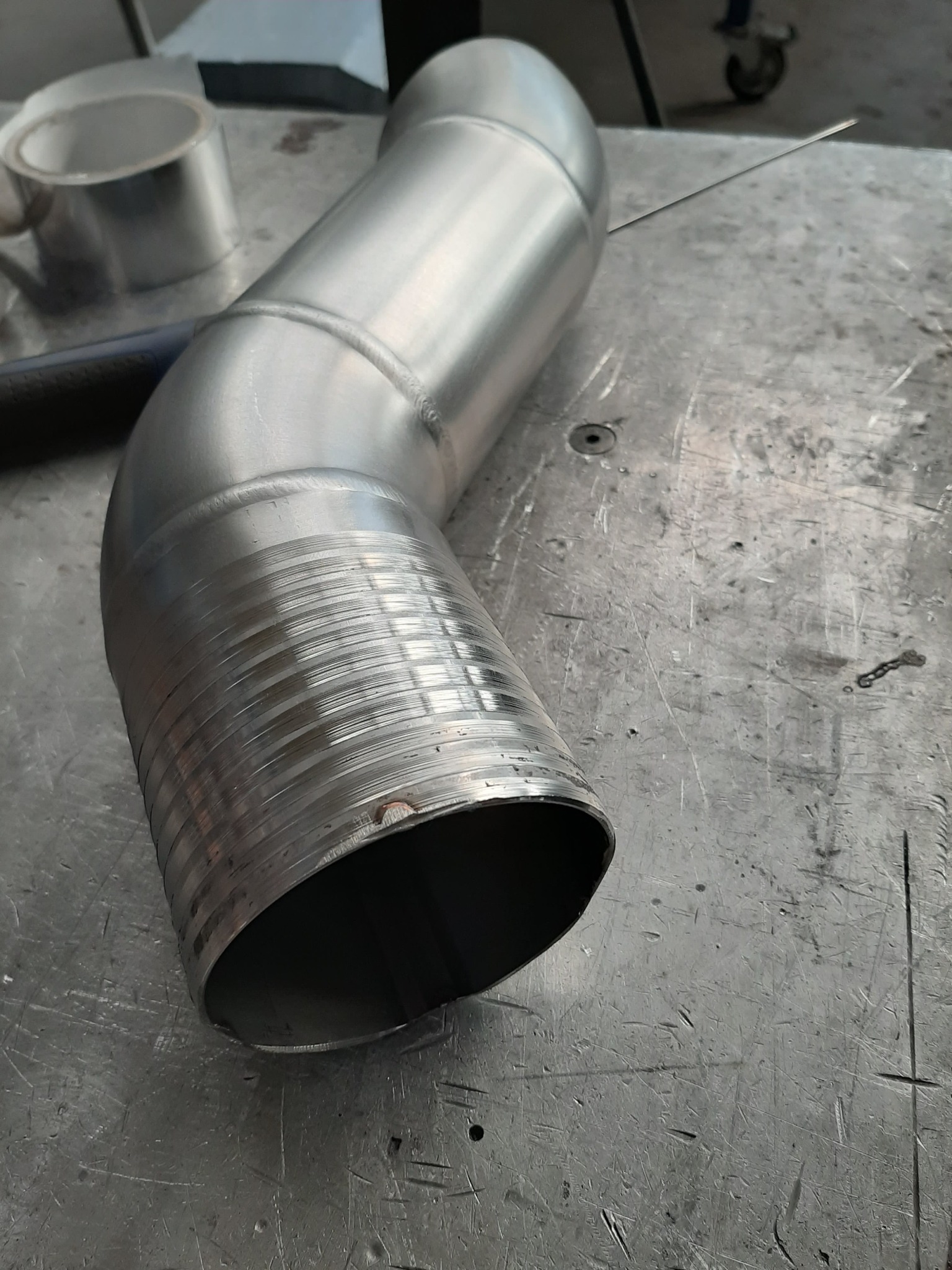 Metalowy, spawany kolankowy element rurowy na roboczym stole ślusarskim, widoczne ślady obróbki i spawania