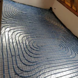 Montaż ogrzewania podłogowego: niebieskie rury grzewcze marki Keller ułożone na srebrnej folii izolacyjnej z widocznymi elementami mocującymi, przygotowane do zalania wylewką, widok z góry.