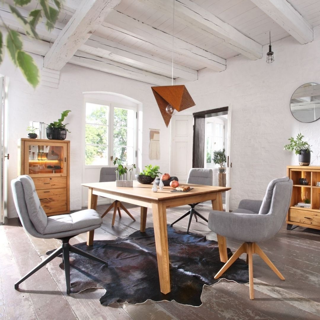 Jadalnia w stylu rustykalnym z drewnianym stołem, szarymi krzesłami na obrotowych podstawach i geometryczną lampą wiszącą z metalu w kolorze rdzy.