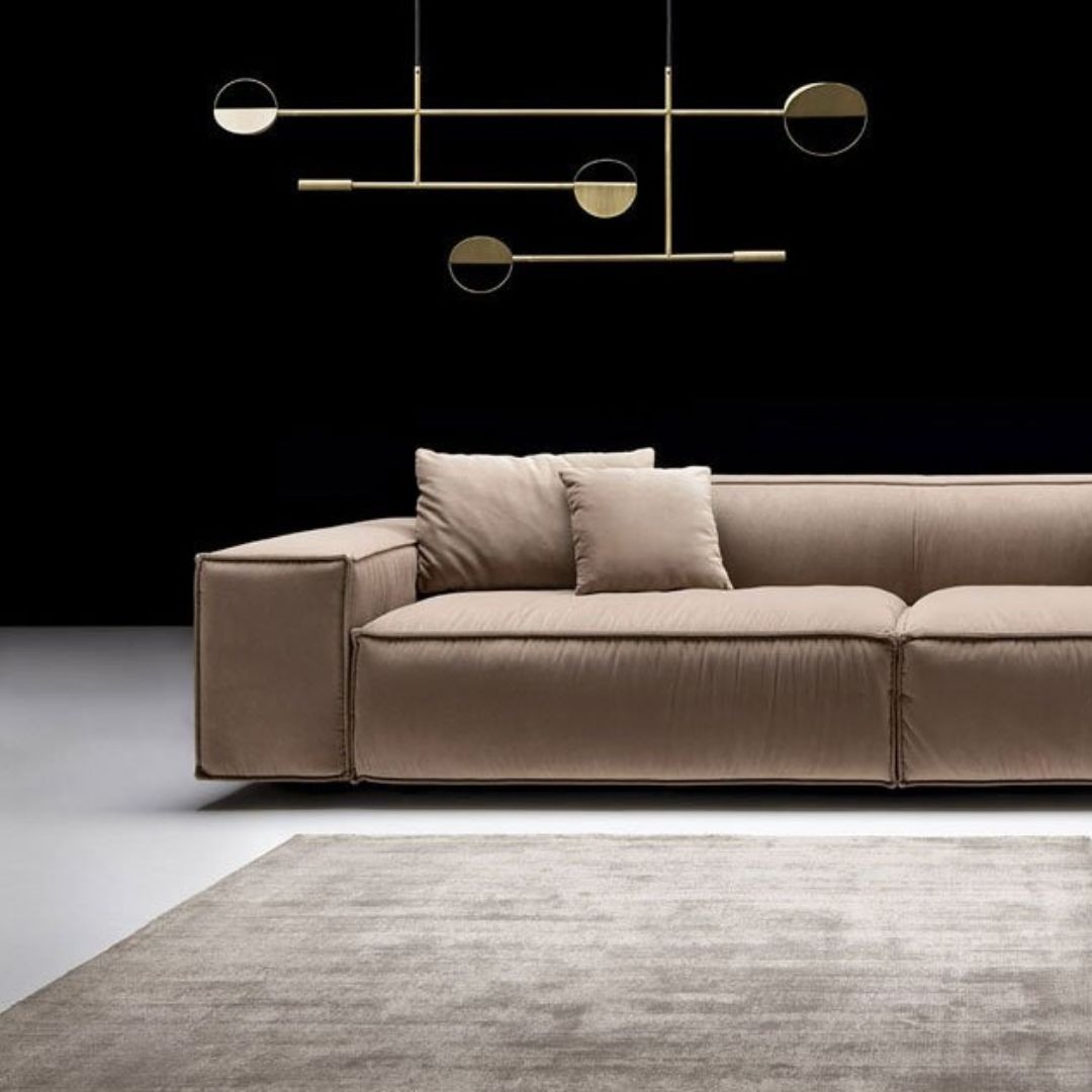 Minimalistyczna lampa wisząca z elementami w kształcie złotych półksiężyców nad beżową sofą i dywanem na tle czarnej ściany.