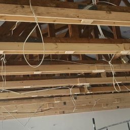 WOODEN - CON SPÓŁKA Z OGRANICZONĄ ODPOWIEDZIALNOŚCIĄ - Wnętrze w trakcie prac wykończeniowych: widok na drewniany szkielet dachu z widocznymi przewodami elektrycznymi, częściowo zakryty płytami kartonowo-gipsowymi.