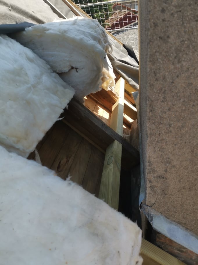 Fragment dachu w trakcie prac: widoczna izolacja z wełny mineralnej, drewniana konstrukcja więźby dachowej i fragment komina z szarego kamienia.