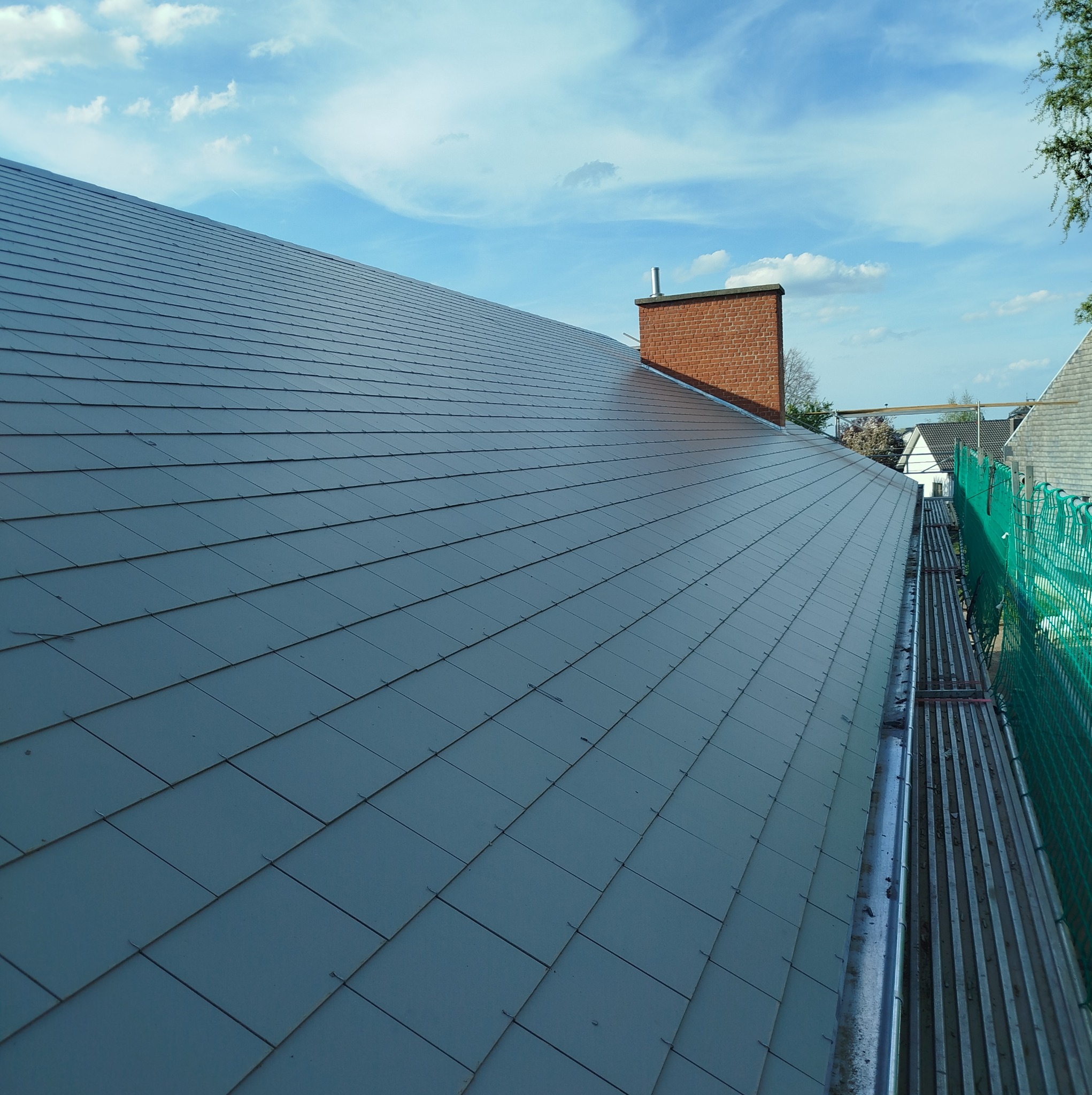 Nowy, grafitowy dach z dachówki bitumicznej, widok z góry, z kominem i rynną. Ujęcie podkreśla regularność wzoru i estetykę wykonania.