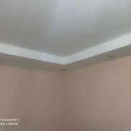 Fragment wnętrza z wykończonym, białym, podwieszanym sufitem i listwą oświetleniową LED, na tle beżowych ścian.