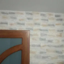 Ściana wykończona panelami imitującymi kamień, widoczny fragment drewnianej ościeżnicy z szybą. W dolnym rogu widoczny biały włącznik światła.