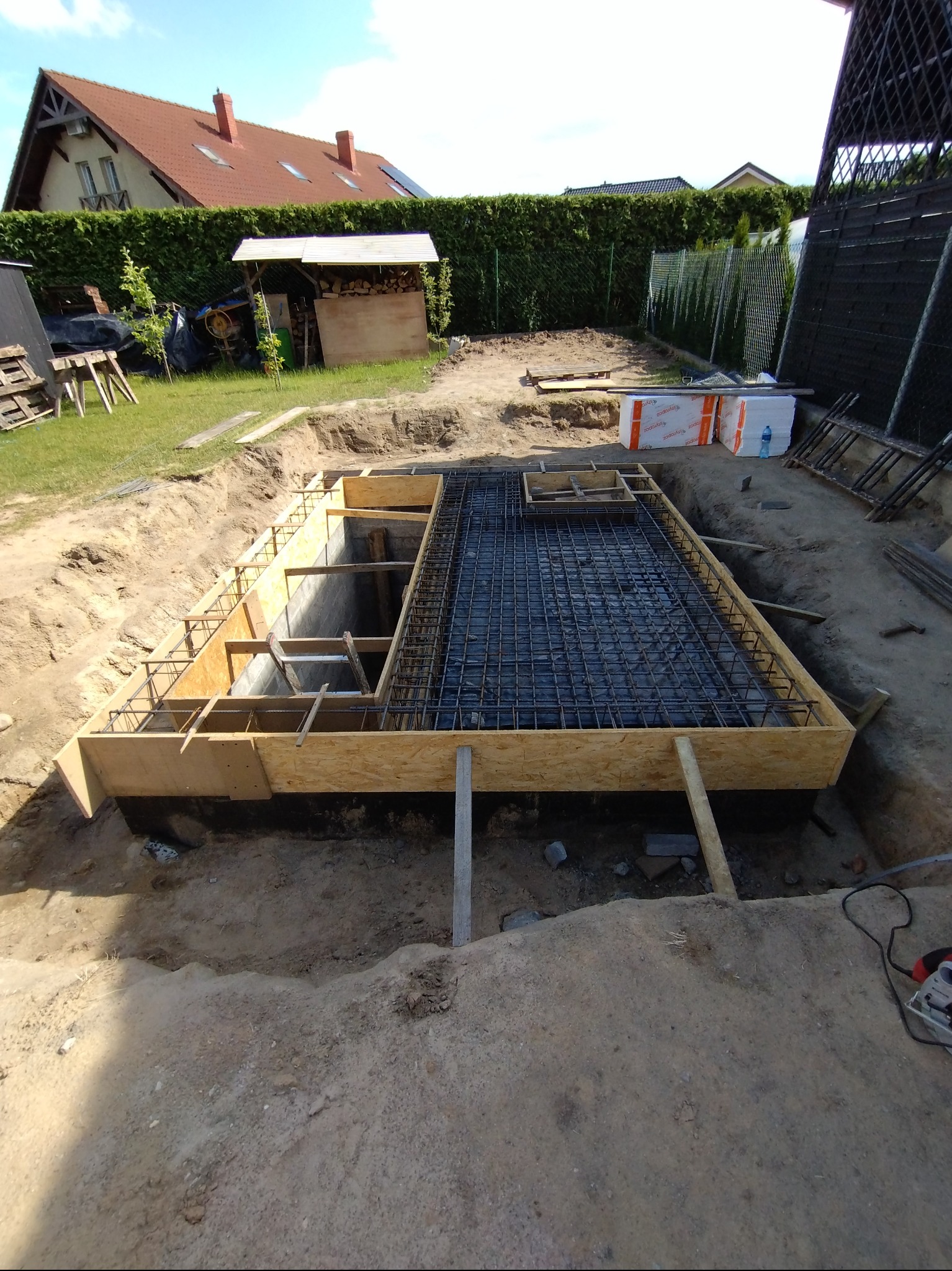 Przygotowanie zbrojenia i szalunku pod płytę fundamentową w Pobiedziskach, widoczna siatka zbrojeniowa i drewniane deskowanie.