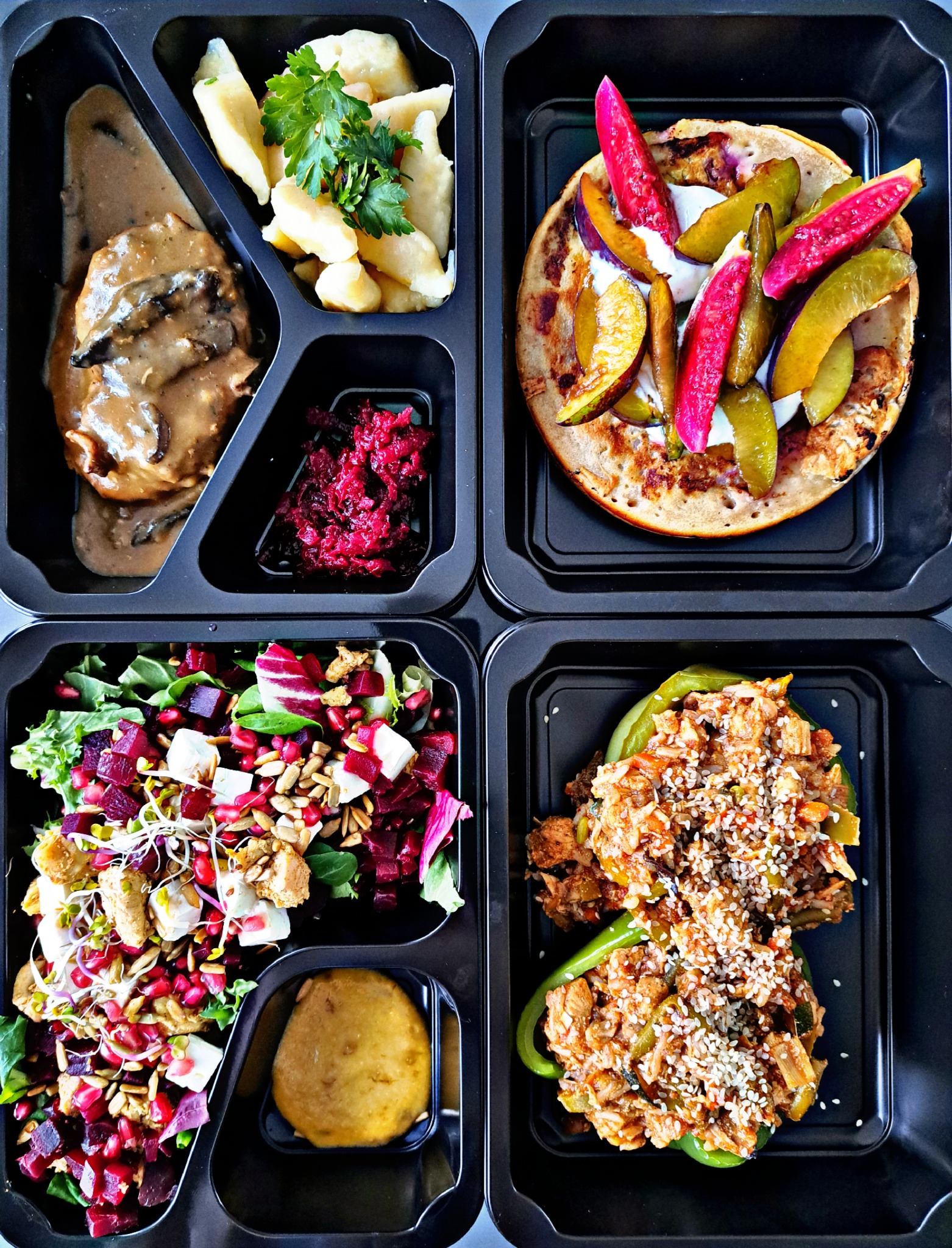 Czterodaniowy posiłek w czarnym, dzielonym pojemniku: kotlet w sosie grzybowym z kopytkami i buraczkami, naleśnik z owocami i kremem, sałatka z buraków, sera i granatu, papryka faszerowana z mięsem...