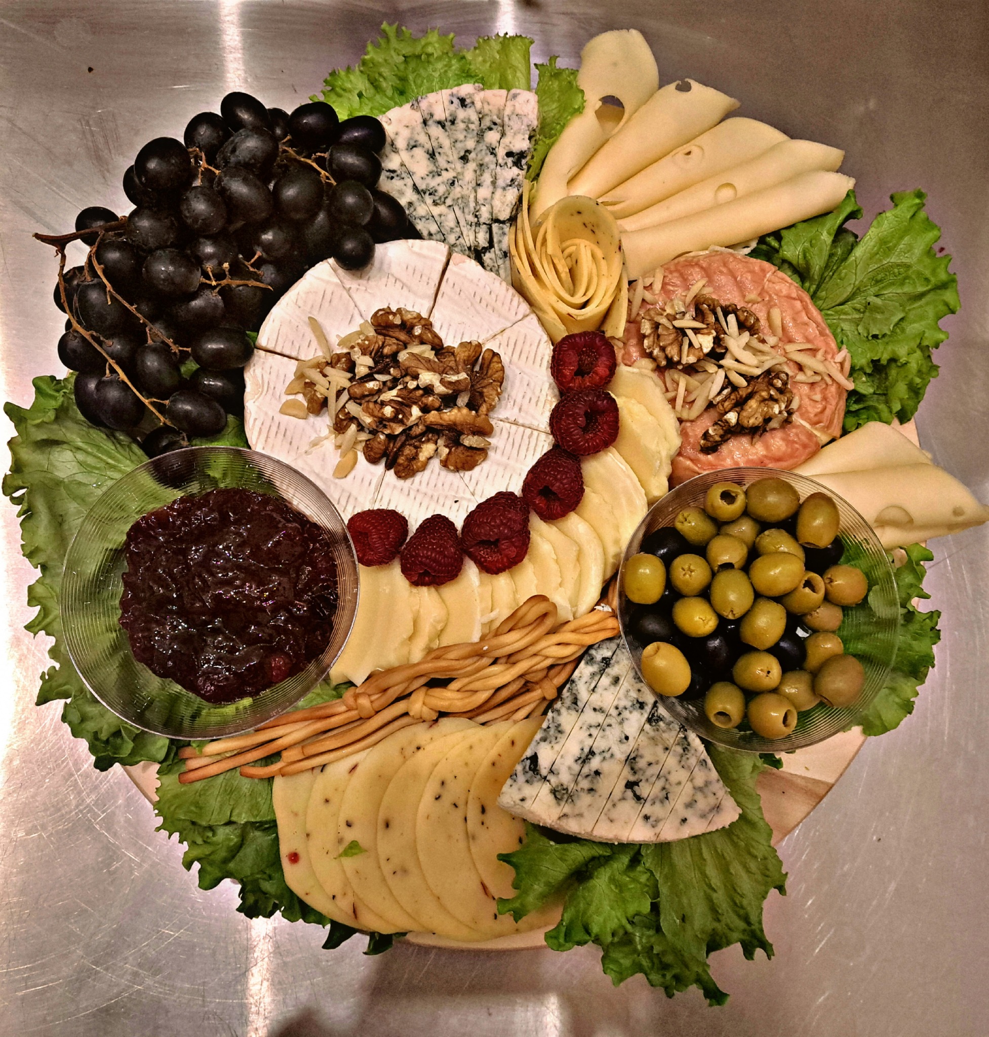 Dekoracyjna deska serów z różnymi gatunkami, orzechami, dżemem, oliwkami, winogronami i malinami na podkładzie z sałaty.