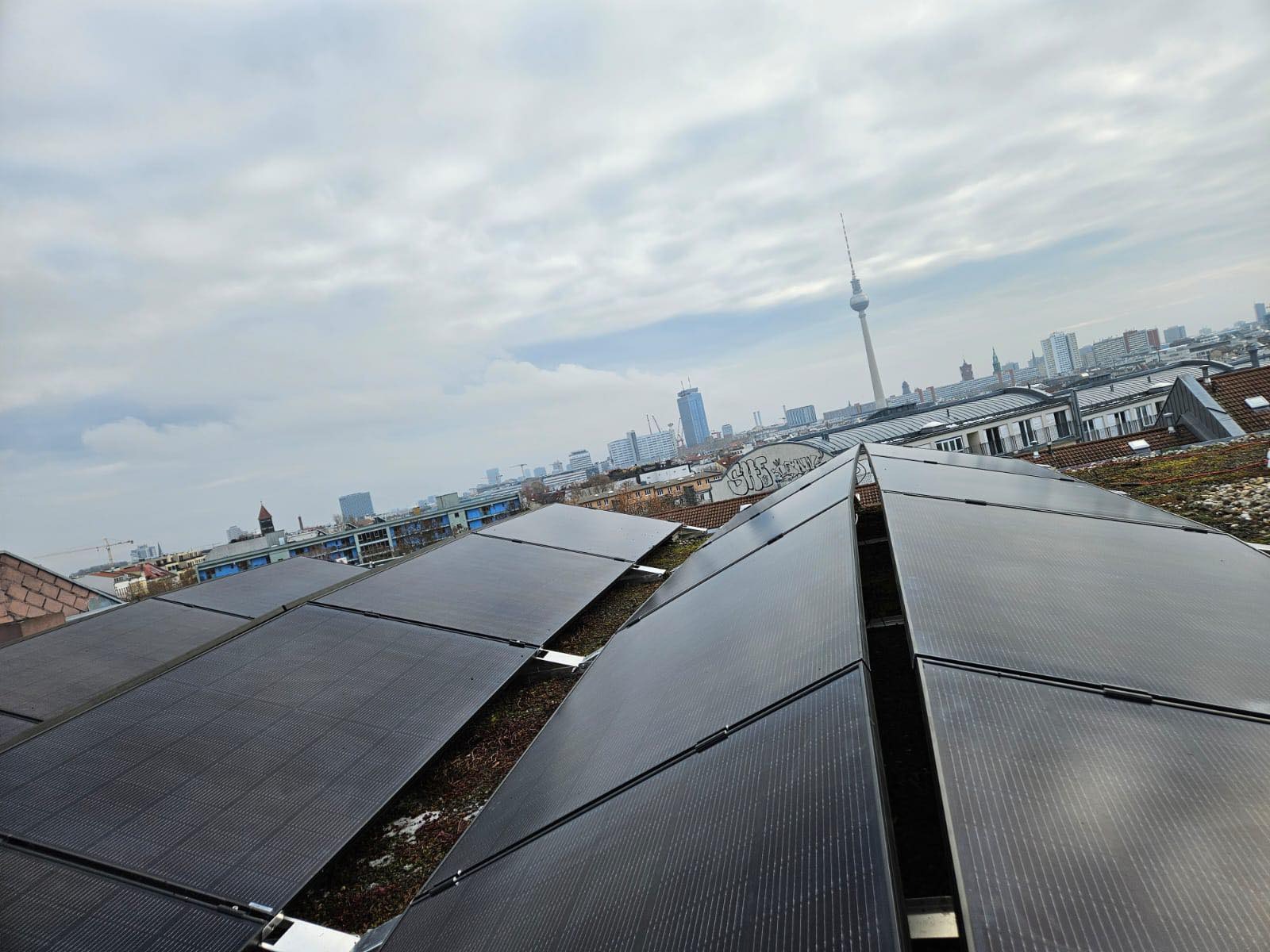 Panele słoneczne na dachu budynku z widokiem na panoramę miasta, w tle wieża telewizyjna w Berlinie.