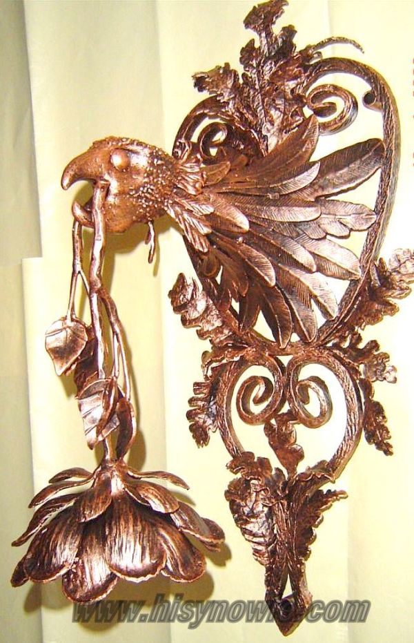 Ręcznie kuta, miedziana dekoracja ścienna przedstawiająca ptaka trzymającego w dziobie kwiat, wykonana w stylu kowalstwa artystycznego.