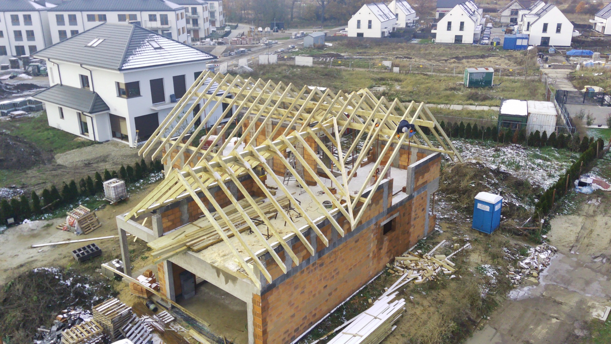 Montaż drewnianej konstrukcji dachu na budynku w stanie surowym otwartym, widok z góry, w tle zabudowa osiedlowa.