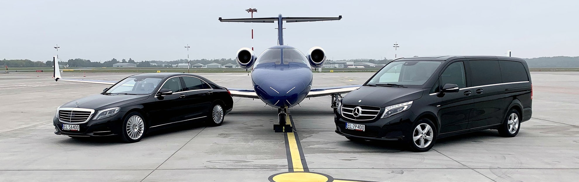 Luksusowa limuzyna Mercedes S-klasy i czarny van Mercedes V-klasy stoją obok prywatnego odrzutowca na płycie lotniska, oferując ekskluzywny transport.