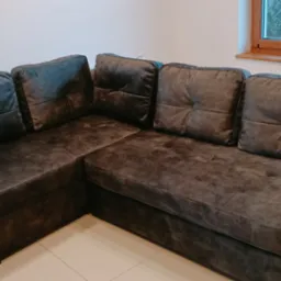 Narożna sofa w odcieniach szarości z kwadratowymi poduszkami, obok okna i choinki świątecznej.