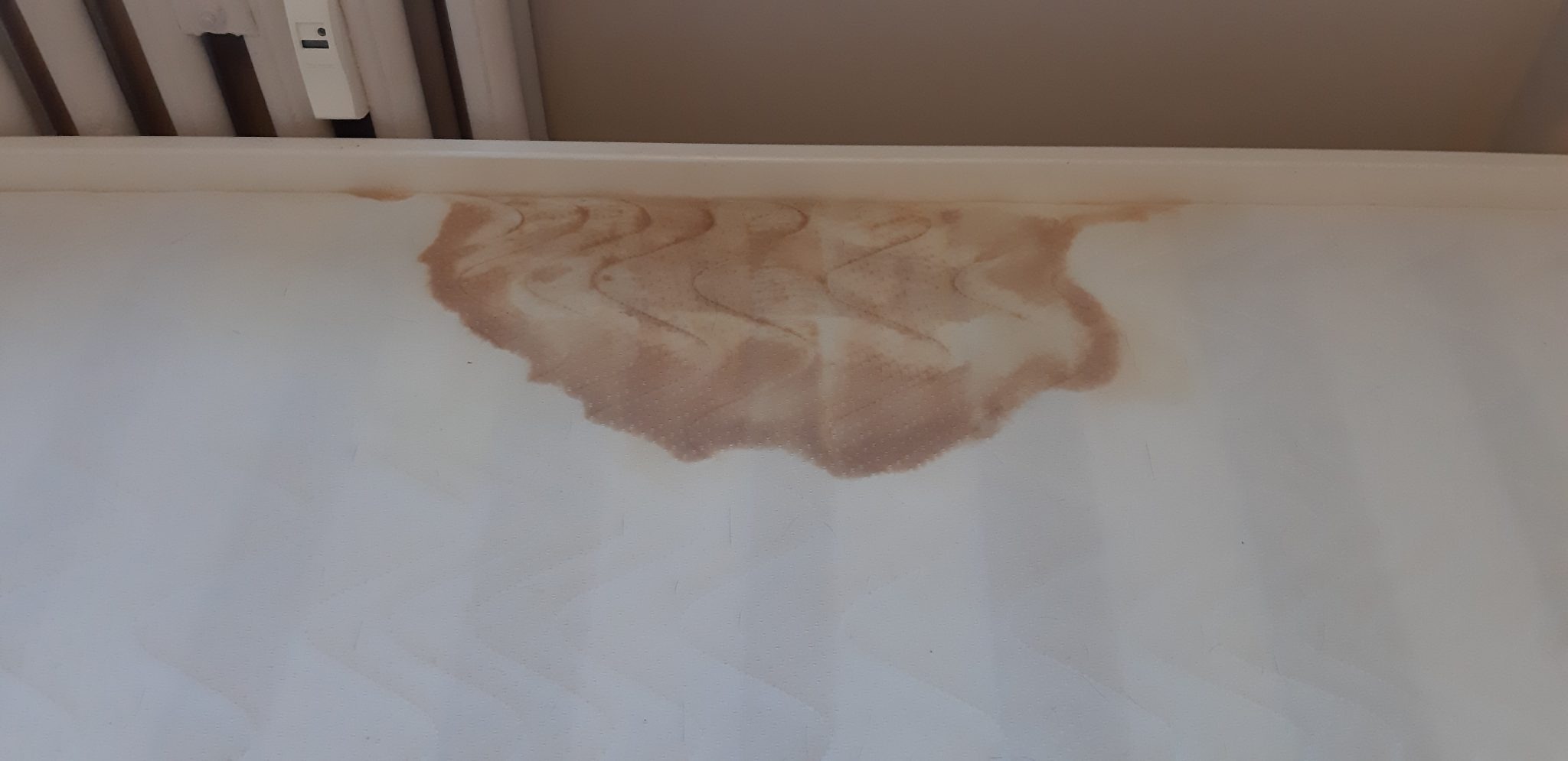 Brązowe zabrudzenie na jasnej, teksturowanej ścianie, prawdopodobnie po zalaniu, z widocznymi śladami spływającej wody.