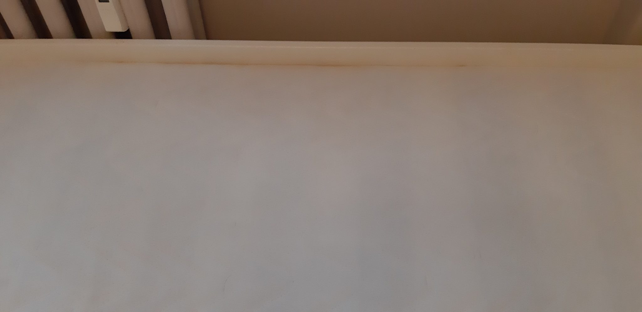 Fragment jasnej tapicerki z widocznymi brązowymi plamami wzdłuż górnej krawędzi, z bliska.