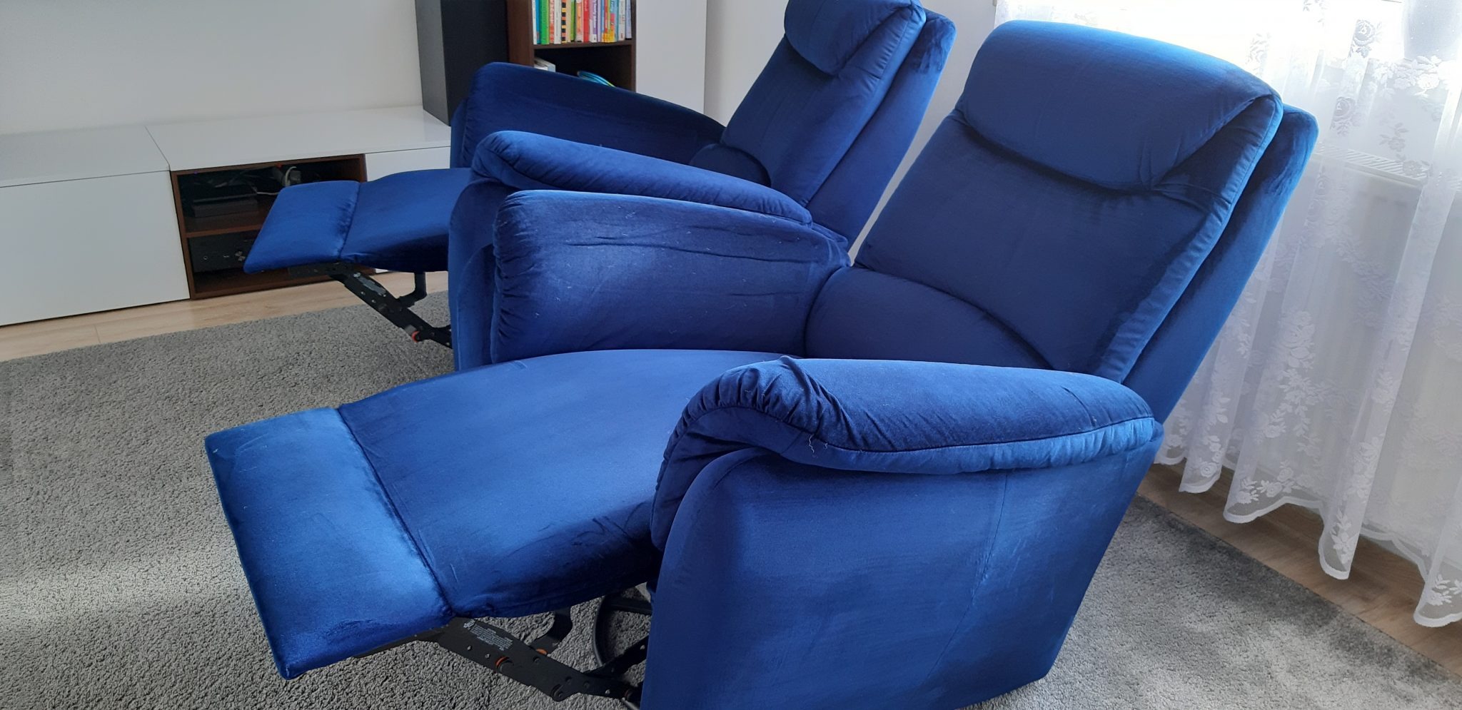 Dwa rozłożone, granatowe fotele tapicerowane z regulacją położenia, na szarym dywanie, widoczne mechanizmy regulacji.