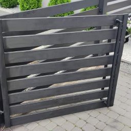 ParvisWelder - Ciemnoszara furtka ogrodzeniowa z poziomych paneli, zamontowana na posesji z kostki brukowej, widoczne schody wejściowe do domu i dekoracyjne krzewy.