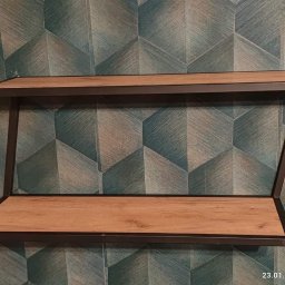 ParvisWelder - Dwu-poziomowa półka ścienna z drewnianymi blatami i metalową ramą, zamontowana na ścianie z geometryczną tapetą w odcieniach zieleni i szarości.