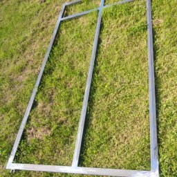 ParvisWelder - Surowa, spawana, metalowa rama bramy wjazdowej leży na trawie, widoczne spawy i zaczepy, przygotowana do dalszej obróbki.