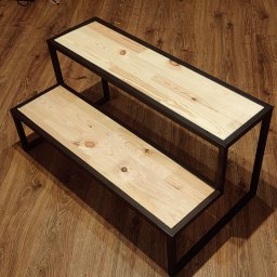 ParvisWelder - Dwupoziomowy kwietnik z jasnego drewna i czarnej metalowej ramy, widoczny na podłodze imitującej drewno.