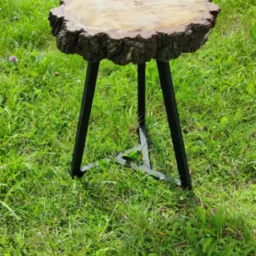 Stolik kawowy z blatem z plastra drewna z korą i czarnymi, metalowymi nogami ustawiony na trawie.