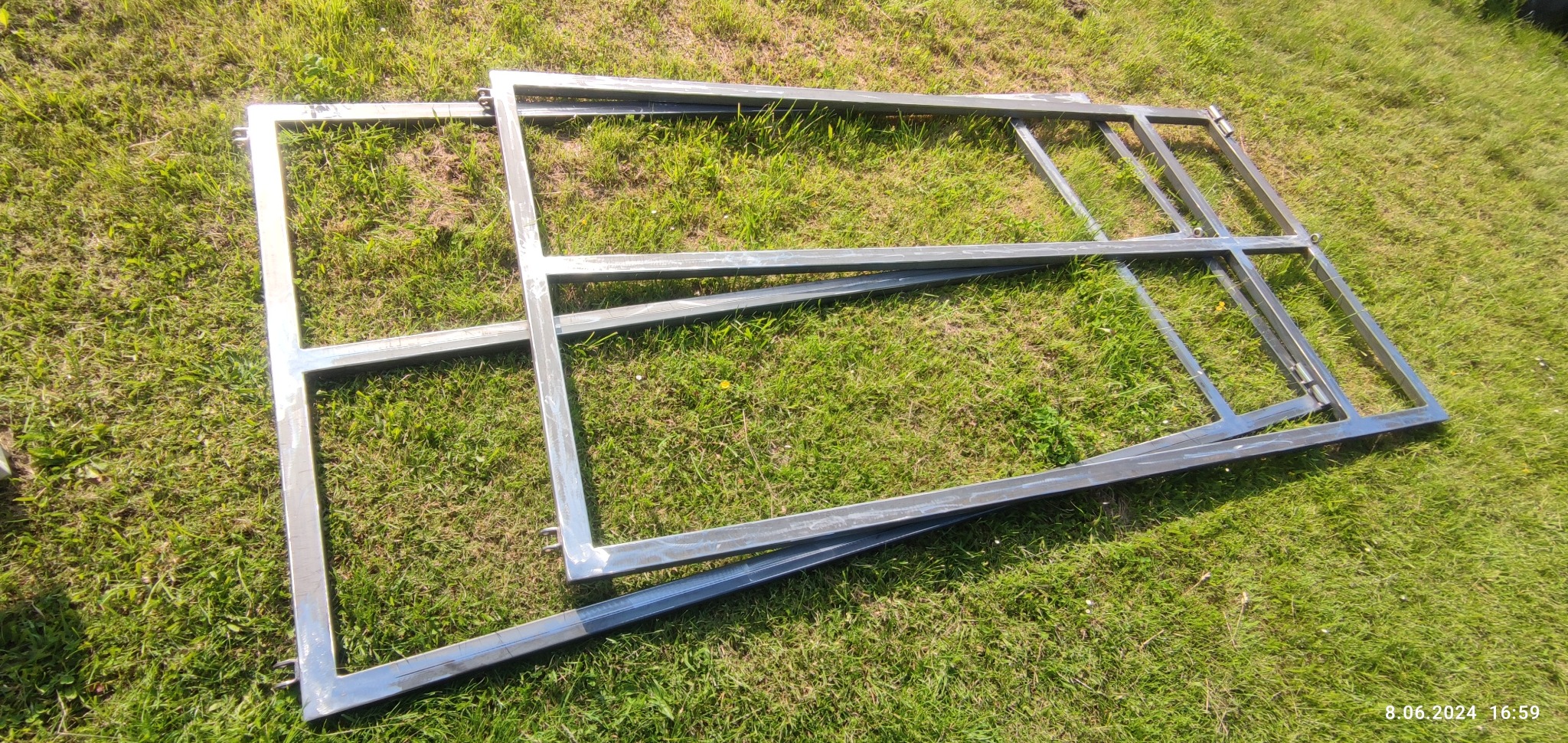 Surowe, spawane ramy metalowe na trawie, widoczne ślady spawania i niedoskonałości, przygotowane do dalszej obróbki lub montażu.