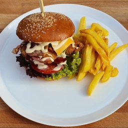 Pizzeria Papay Legionowo - Apetyczny burger z frytkami na białym talerzu, widoczne warstwy: sałata, pomidor, cebula, panierowany kotlet, bekon, ser i sos; burger spięty wykałaczką.