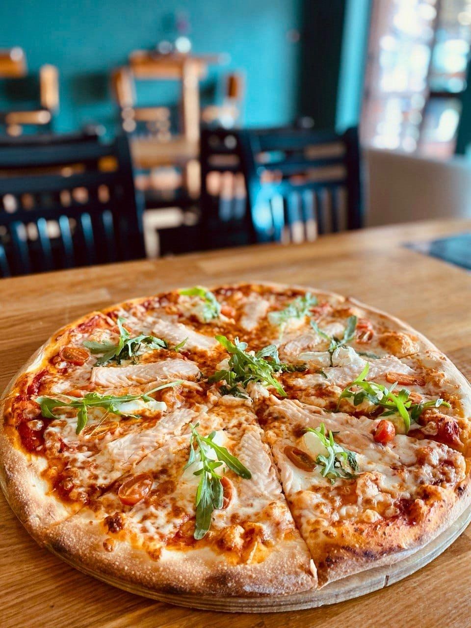 Pizza z łososiem, rukolą i pomidorkami koktajlowymi na drewnianym stole w restauracji.