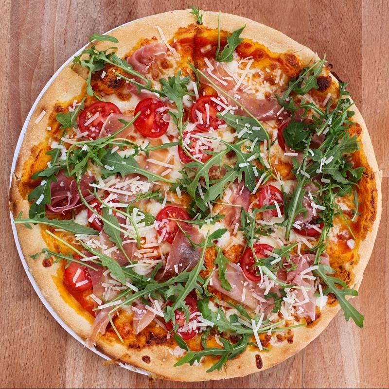 Pizza z szynką parmeńską, pomidorkami cherry, rukolą i parmezanem na cienkim cieście, serwowana w Legionowie.