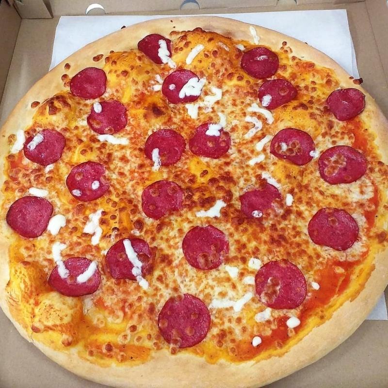 Okrągła pizza pepperoni w kartonowym pudełku, z widocznymi plamkami sera i sosem pomidorowym.