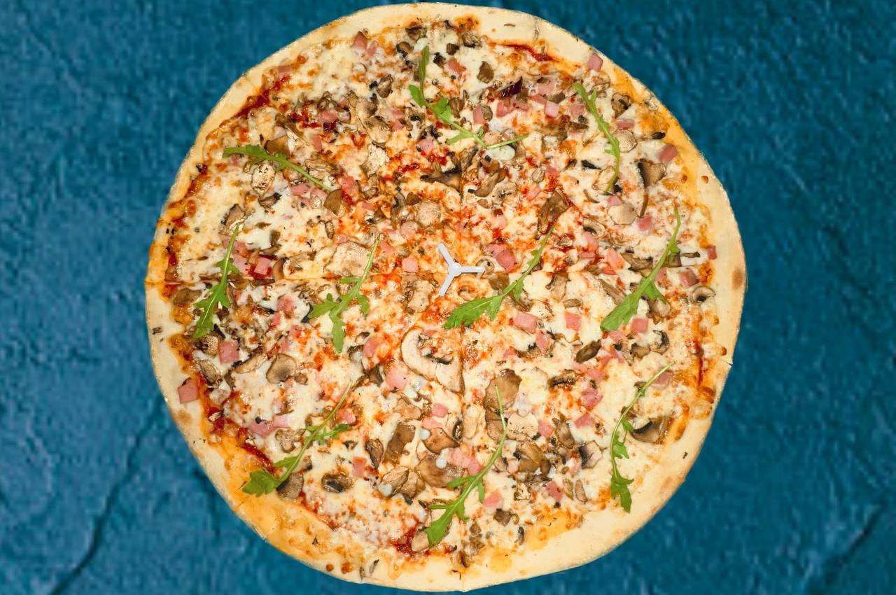 Okrągła pizza z pieczarkami, szynką i rukolą na niebieskim tle z widocznym plastikowym trójnożnym dystansem w centrum.