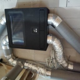 Kamil Wojtalik Klarvent - Zamontowany rekuperator z widocznymi przewodami wentylacyjnymi, złączami i elementami mocującymi do ściany z betonu komórkowego.