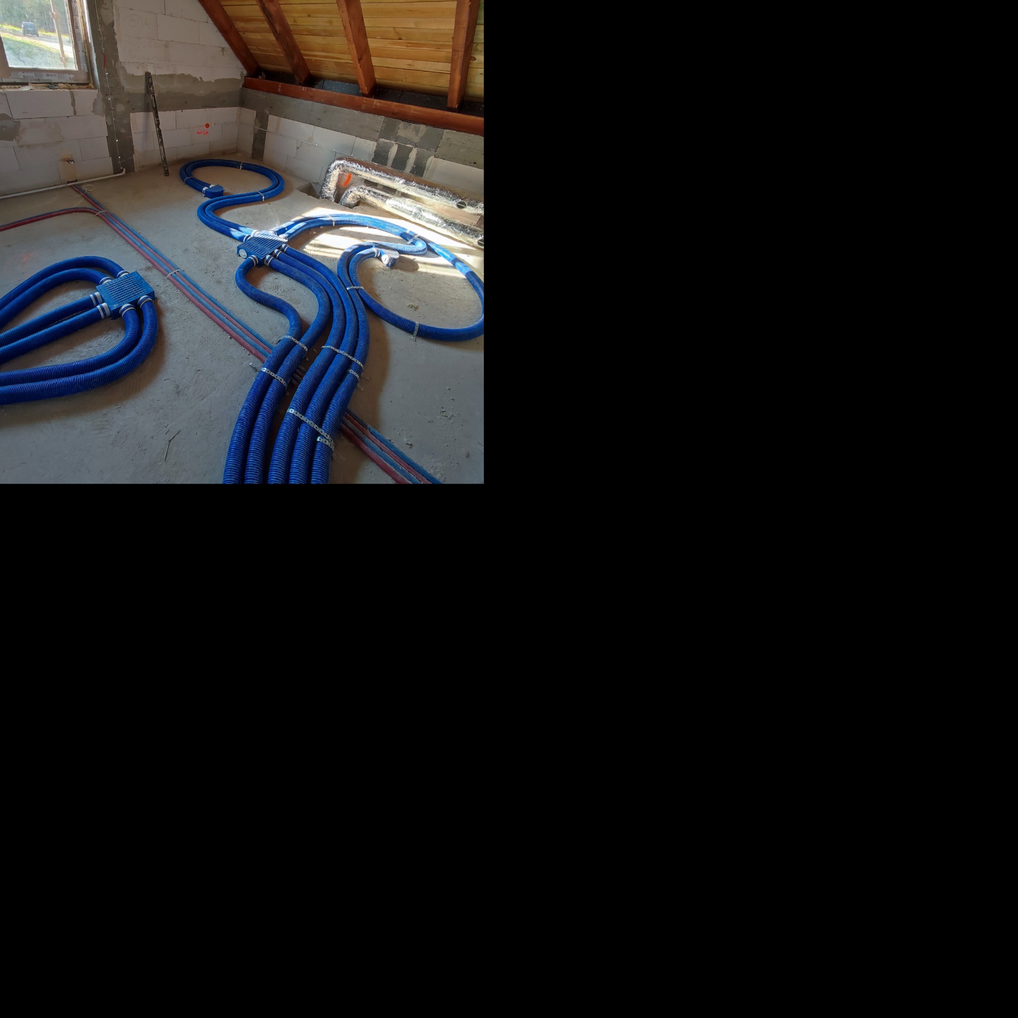 Niebieskie rury wentylacyjne, częściowo przymocowane do surowej podłogi, w trakcie montażu w nowym budynku z widocznym oknem i konstrukcją dachu.