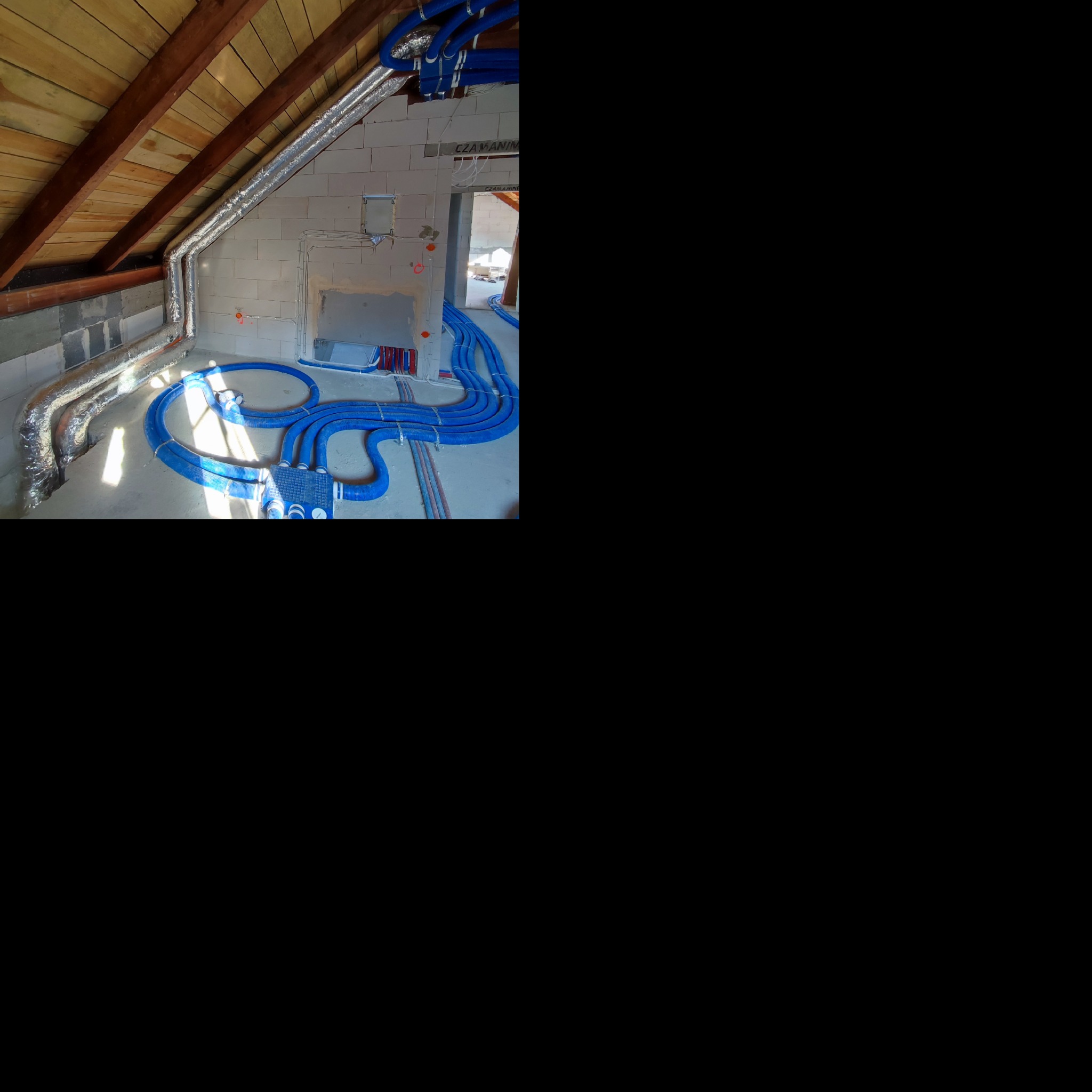 Rozprowadzenie niebieskich rur wentylacyjnych na poddaszu, widoczne także aluminiowe rury wentylacyjne pod stropem z drewnianych belek.