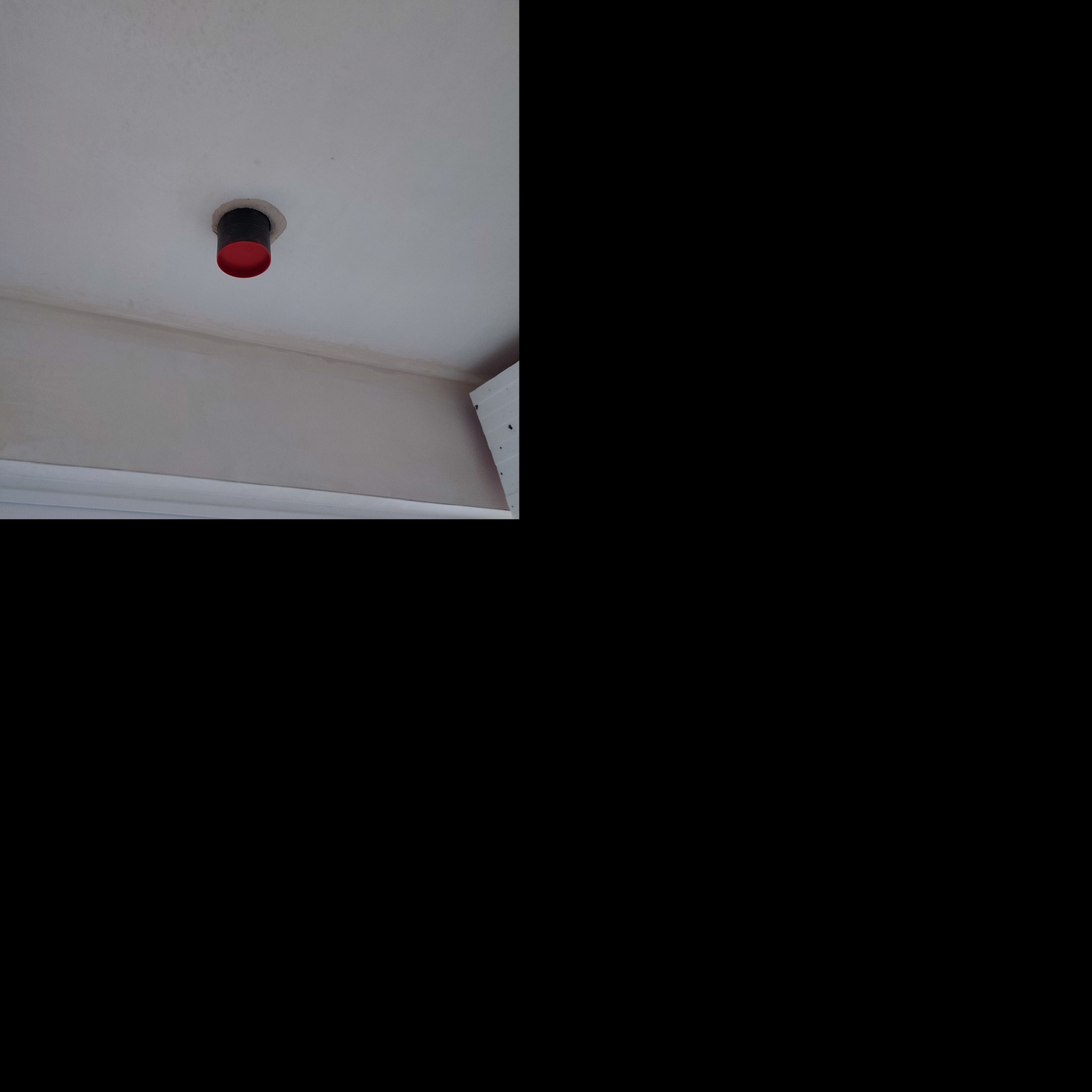 Czerwono-czarny element instalacji wystający z sufitu, otoczony świeżym gipsem.