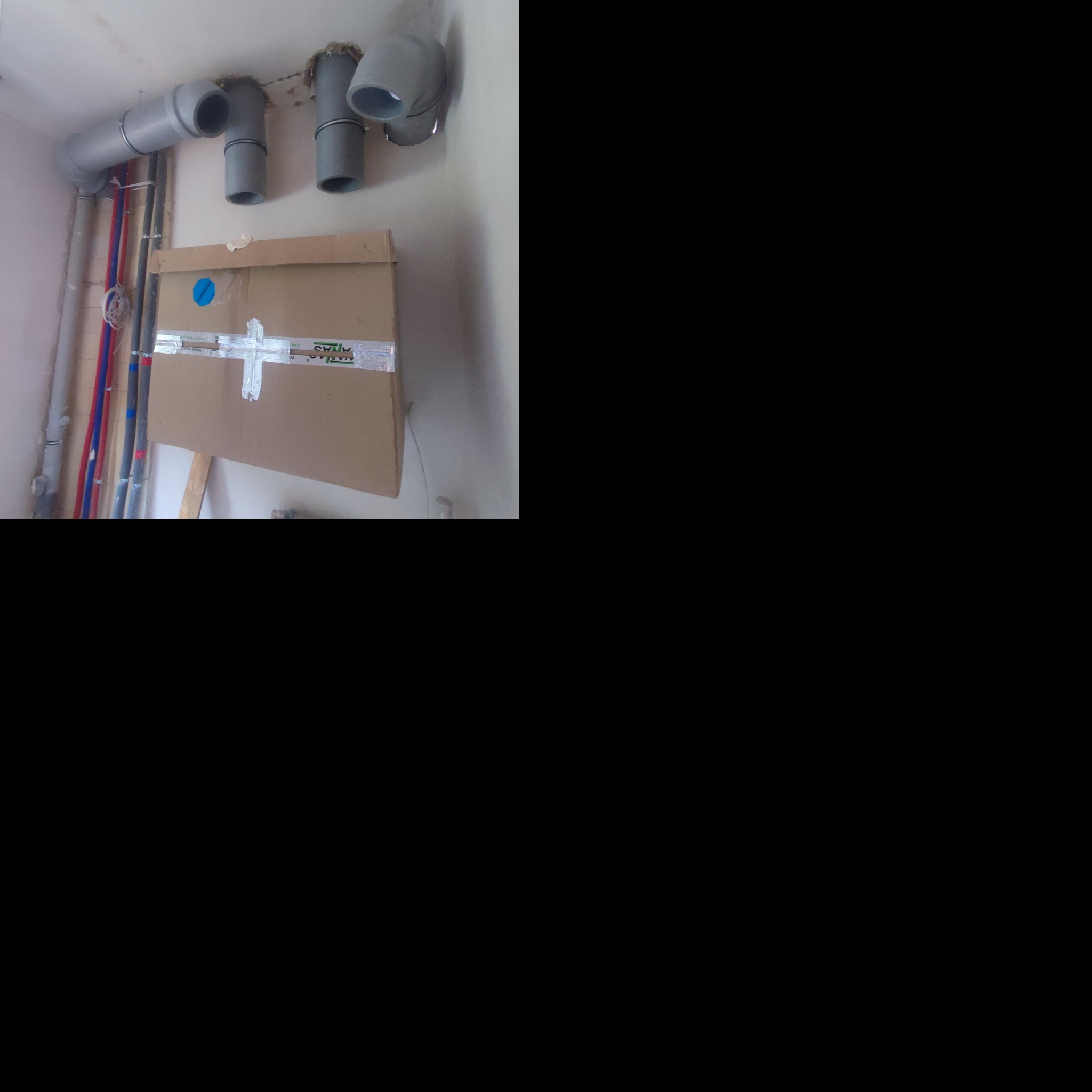 Szare rury wentylacyjne pod sufitem, zabezpieczone kartonem, widoczne rury instalacji wodnej w kolorze czerwonym i niebieskim.