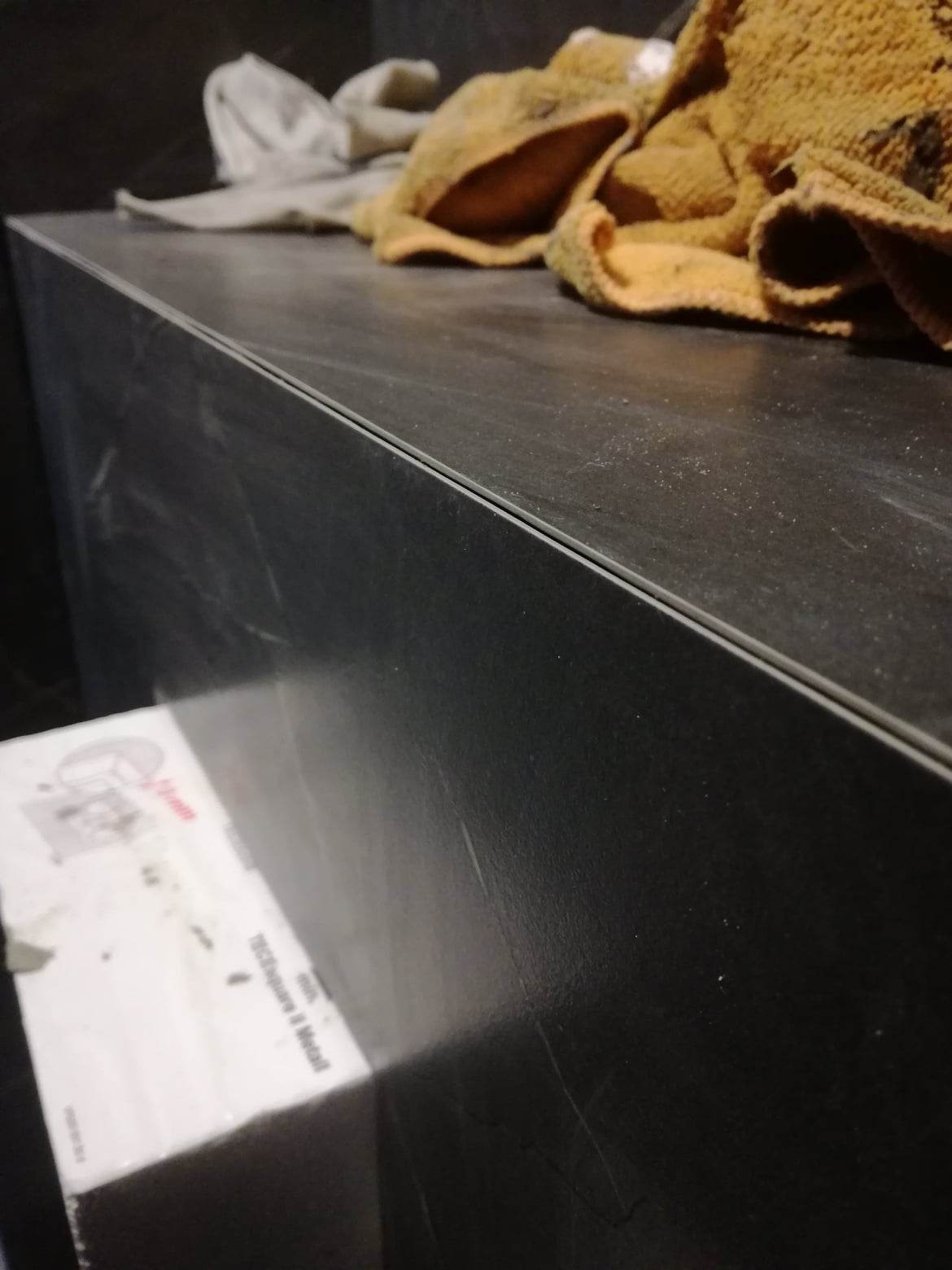 Fragment wykończonej ściany z ciemnych płyt, z widoczną fugą i narzędziami oraz brudnymi ściereczkami na górze, sugerujące prace wykończeniowe w łazience.