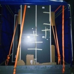 KINGARTKURIER Artur Szyszkowski - Wnętrze skrzyni ładunkowej z niebieską plandeką, zabezpieczone meble numerowane 9, 11, 12, owinięte taśmą klejącą i przymocowane pomarańczowymi pasami transportowymi, kartony na podłodze.