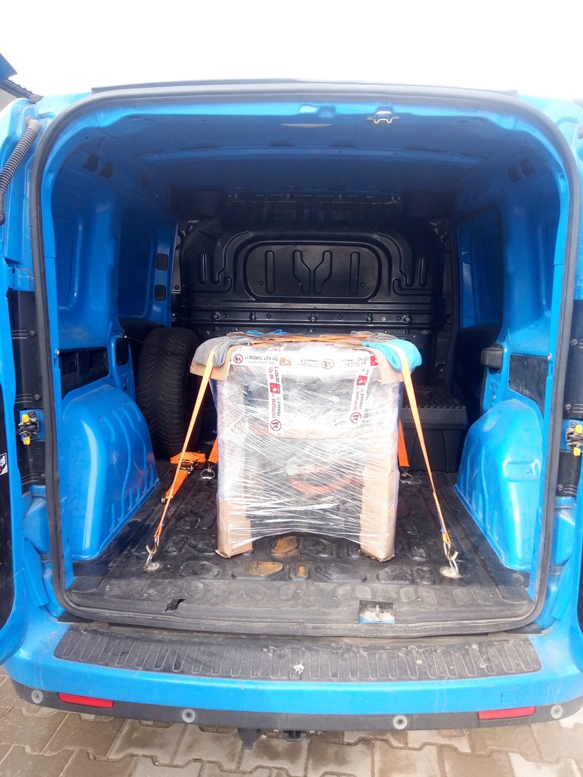 Mebel zabezpieczony folią i pasami transportowymi wewnątrz niebieskiego busa podczas przeprowadzki.