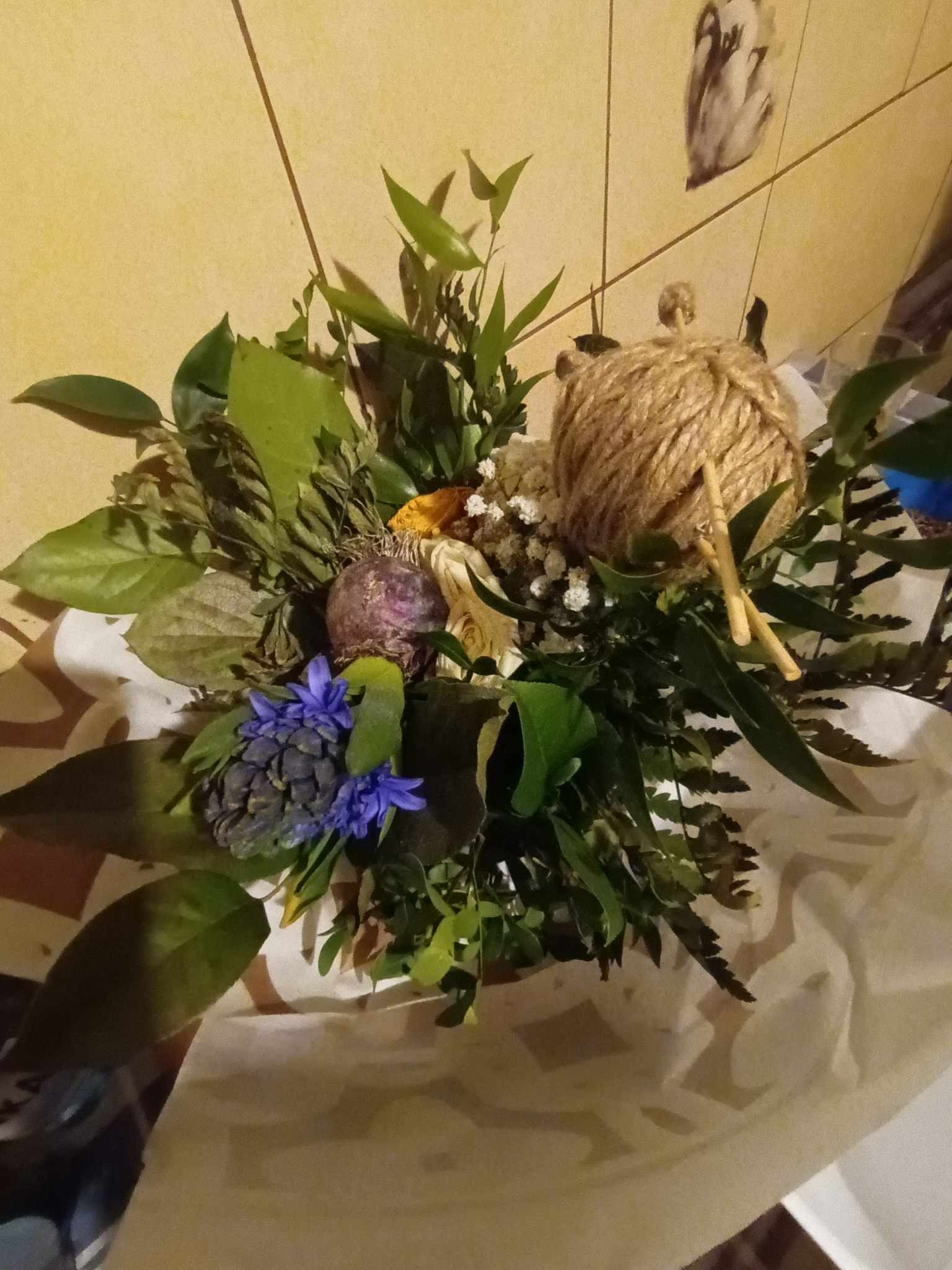 Dekoracyjny bukiet z niebieskimi hiacyntami, zielonymi liśćmi, suszonymi kwiatami i kulą ze sznurka jutowego, umieszczony na białym papierze.