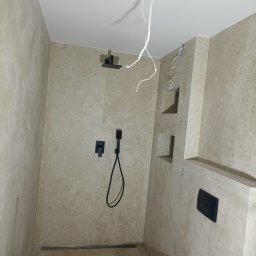 Andrii zubakha - Niedokończona łazienka z beżowymi płytkami, czarną armaturą i wystającymi kablami z sufitu, widoczne wnęki w ścianie.
