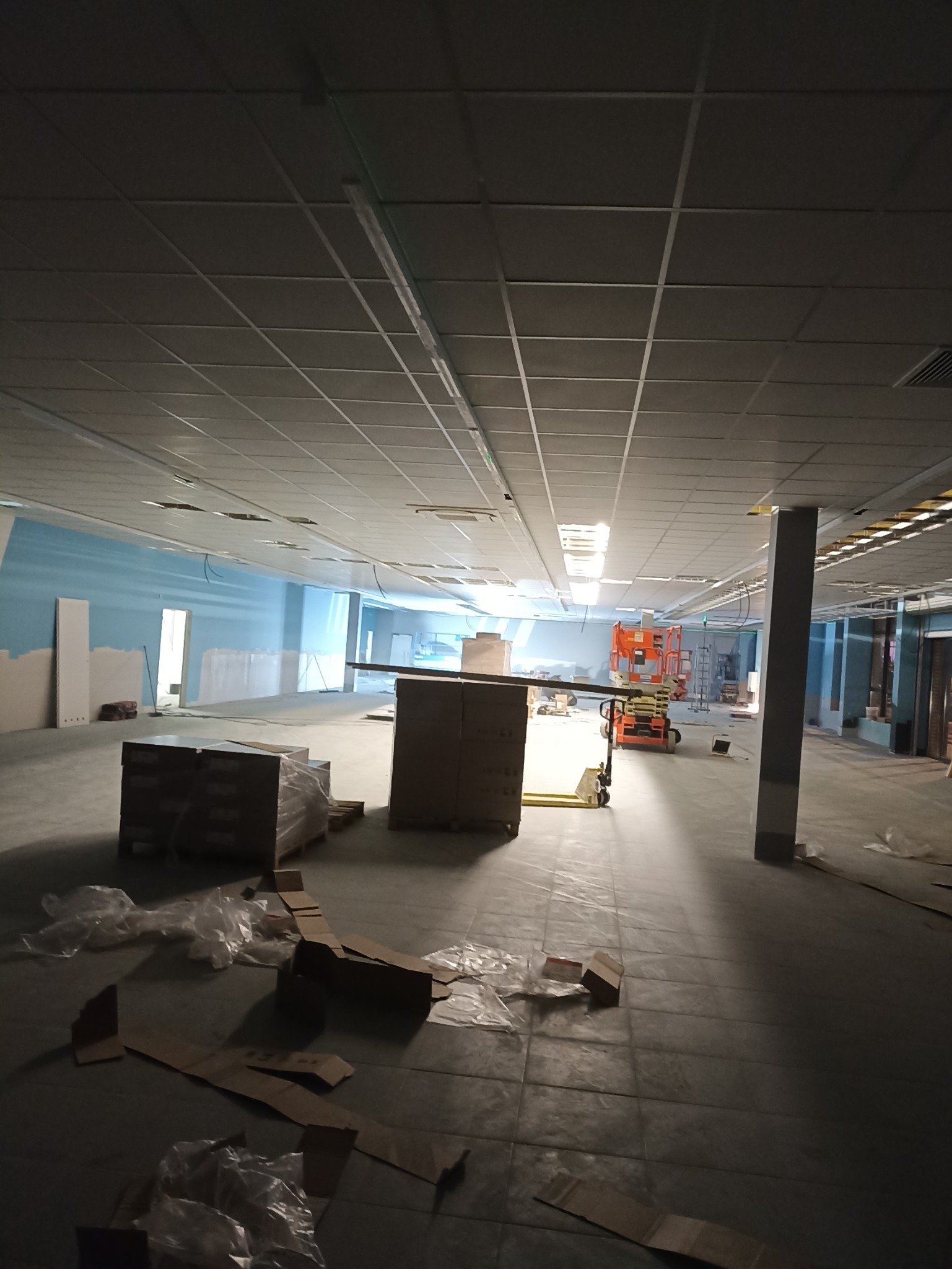 Montaż sufitu podwieszanego z płyt karton-gips w dużym pomieszczeniu, widoczne rusztowania i materiały budowlane.