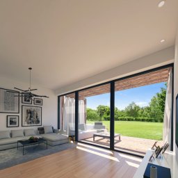 M11 architekci - Wnętrze nowoczesnego salonu z dużym oknem tarasowym wychodzącym na ogród, szara sofa z poduszkami, abstrakcyjna lampa sufitowa i galeria czarno-białych zdjęć na ścianie. Na stoliku kawowym leżą...