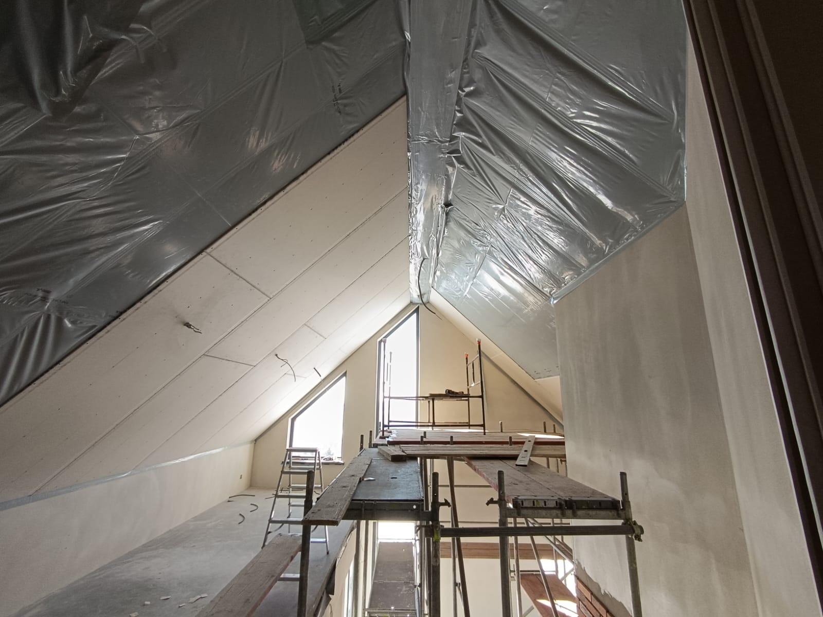 Poddasze w Jaworzynce w trakcie ocieplania, widoczne rusztowania, folia izolacyjna i płyty kartonowo-gipsowe na skośnych ścianach.