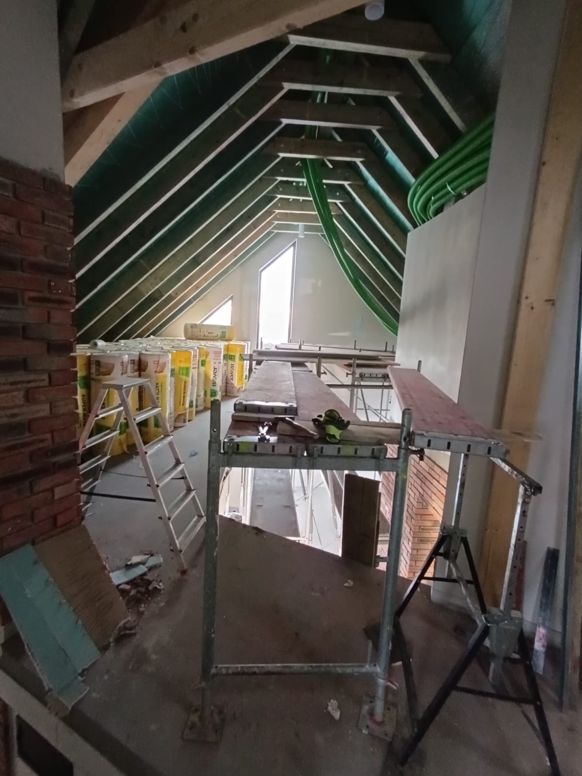 Poddasze w trakcie adaptacji: widoczne ocieplenie w rolkach, rusztowanie, fragment murowanej ściany i instalacja wentylacyjna pod skośnym dachem.