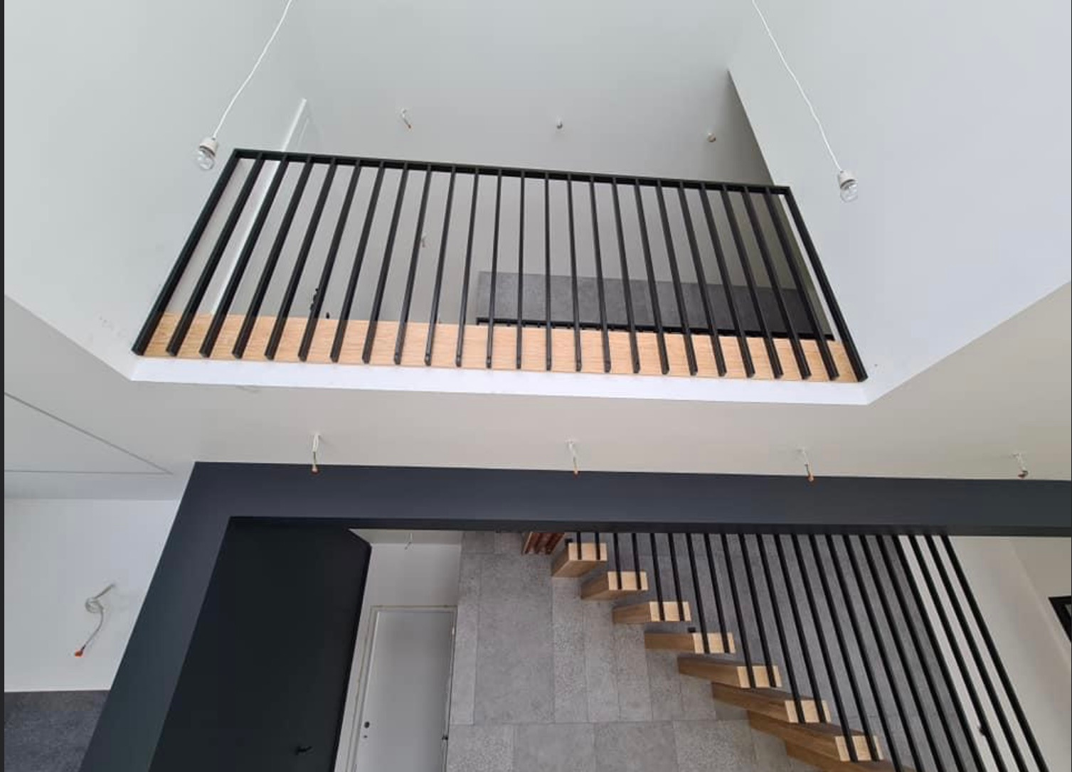 Nowoczesne wnętrze z drewnianymi schodami i czarną metalową balustradą, widok z dołu, szare płytki na ścianie, minimalizm.