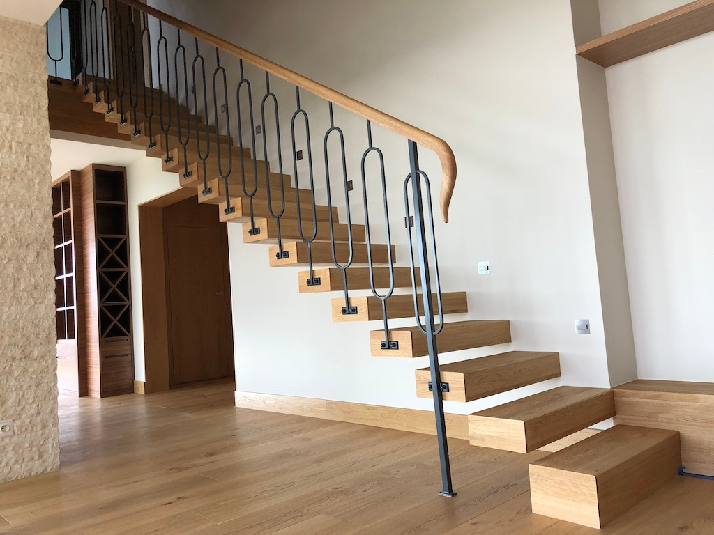 Nowoczesne schody z drewnianymi stopniami i metalową balustradą w jasnym wnętrzu z podłogą z desek.